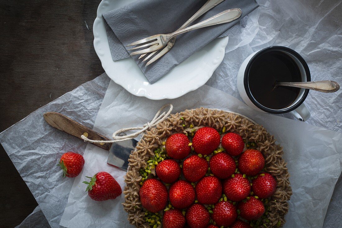 Strawberry tart with ribbon on wooden table with dishes