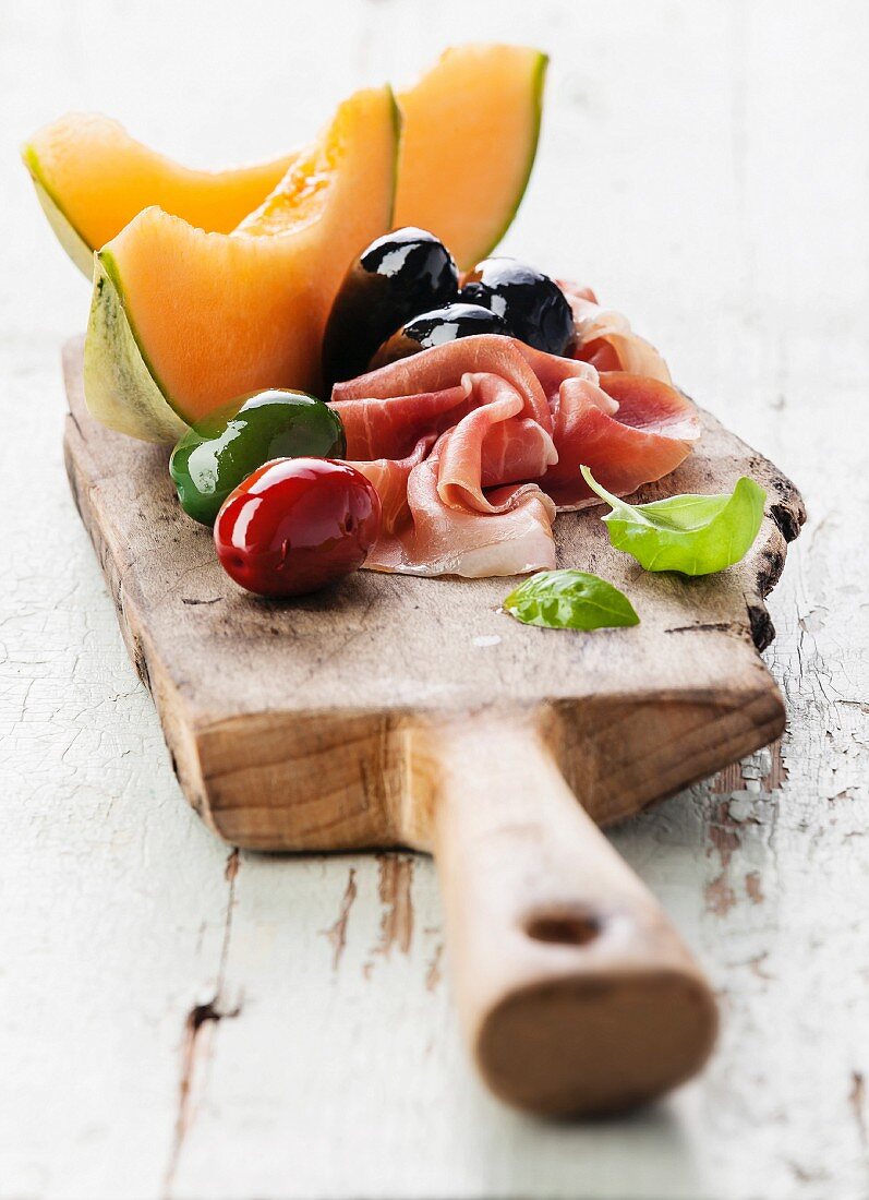 Prosciutto ham, Slices of melon cantaloupe and Olives on cutting board