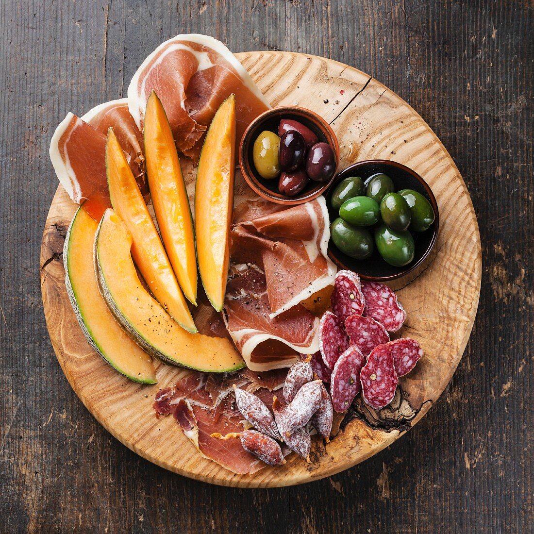 Antipasto ham, melon and olives on wooden background