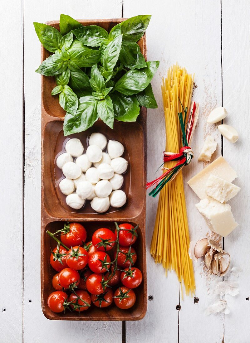 Basilikum, Mozzarella und Tomaten (italienische Flaggenfarben) in Holzschale, daneben Parmesan und Spaghetti