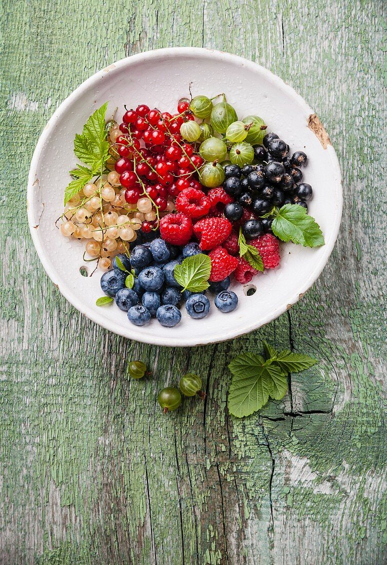 Mix of fresh berries with leaves in vintage ceramic colander on green rustic wooden background