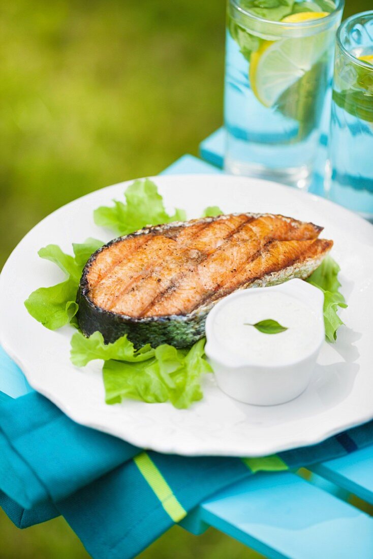 Grilled salmon steak on a fresh green salad with garlic sauce