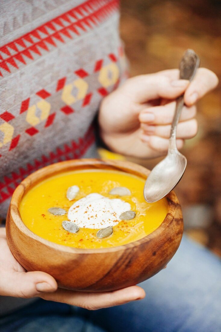 Woman holding pumpkin soup in a rustic bowl outside