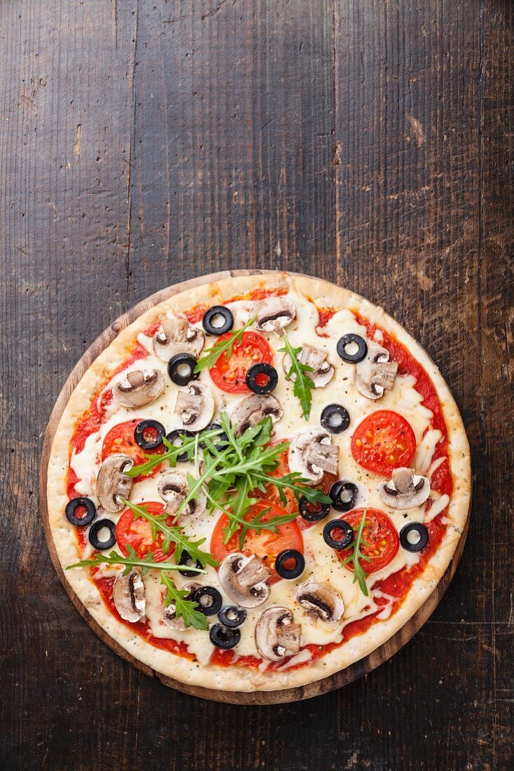 Pizza mit Pilzen, Oliven und Rucola auf Holztisch