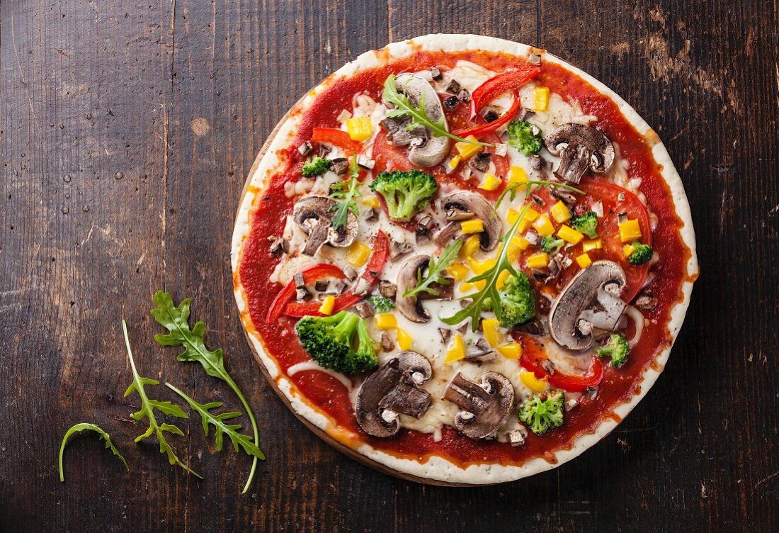 Vegetarische Pizza mit Pilzen und Rucola auf Holztisch