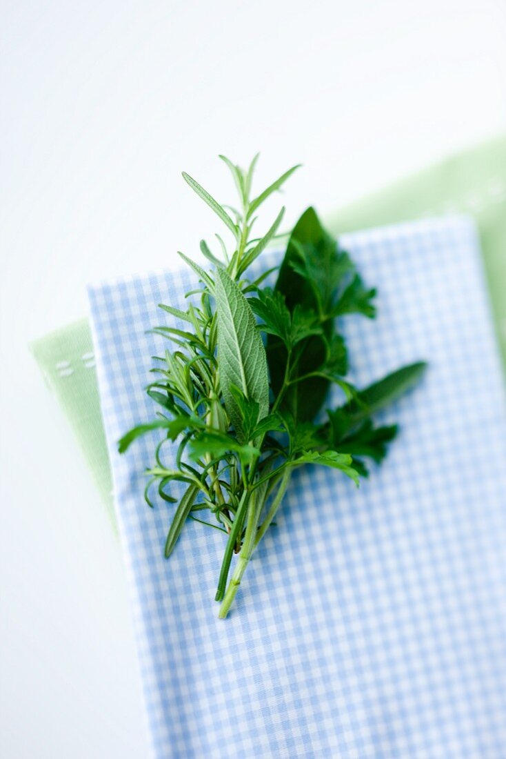 Rosemary, sage and parsley on a blue and white checked napkin