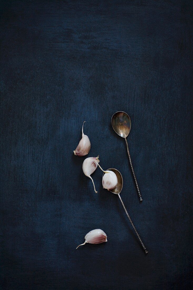 Garlic cloves and vintage silver spoons on a black background