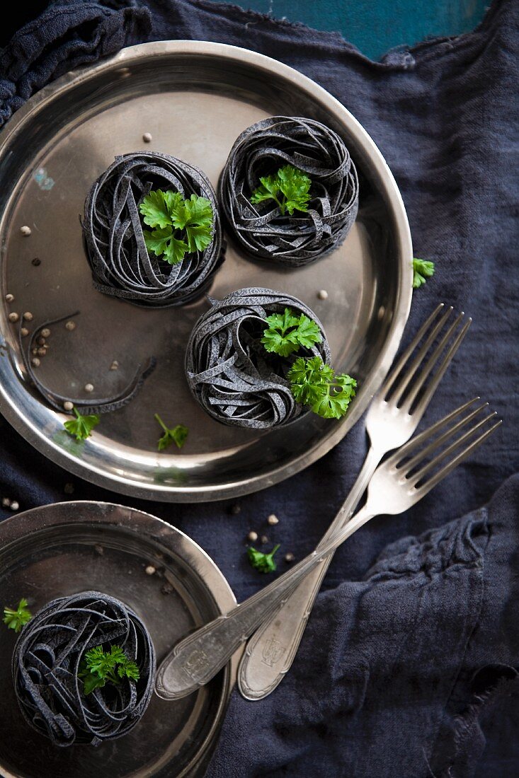 Black ribbon noodles and parsley on a stainless steel plate