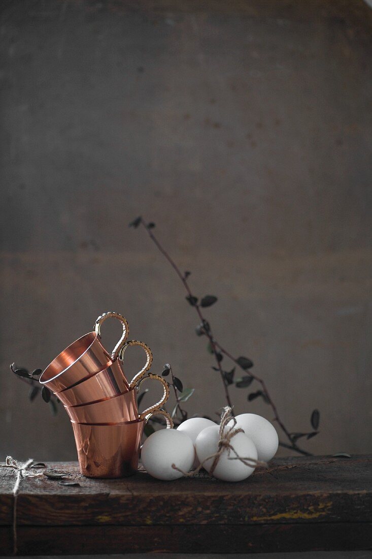 Stacked copper cups and white hen's eggs on wooden table