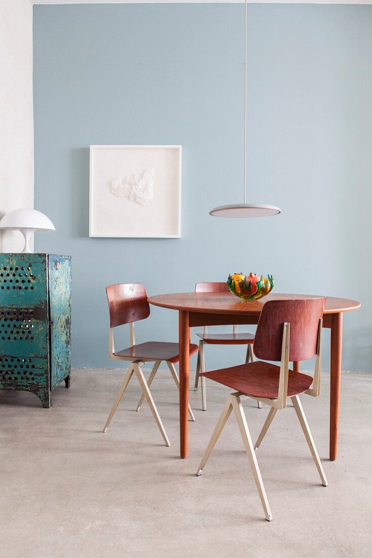 Essplatz mit Retro Tisch und Stühlen und moderner Pendelleuchte vor hellblauer Wand