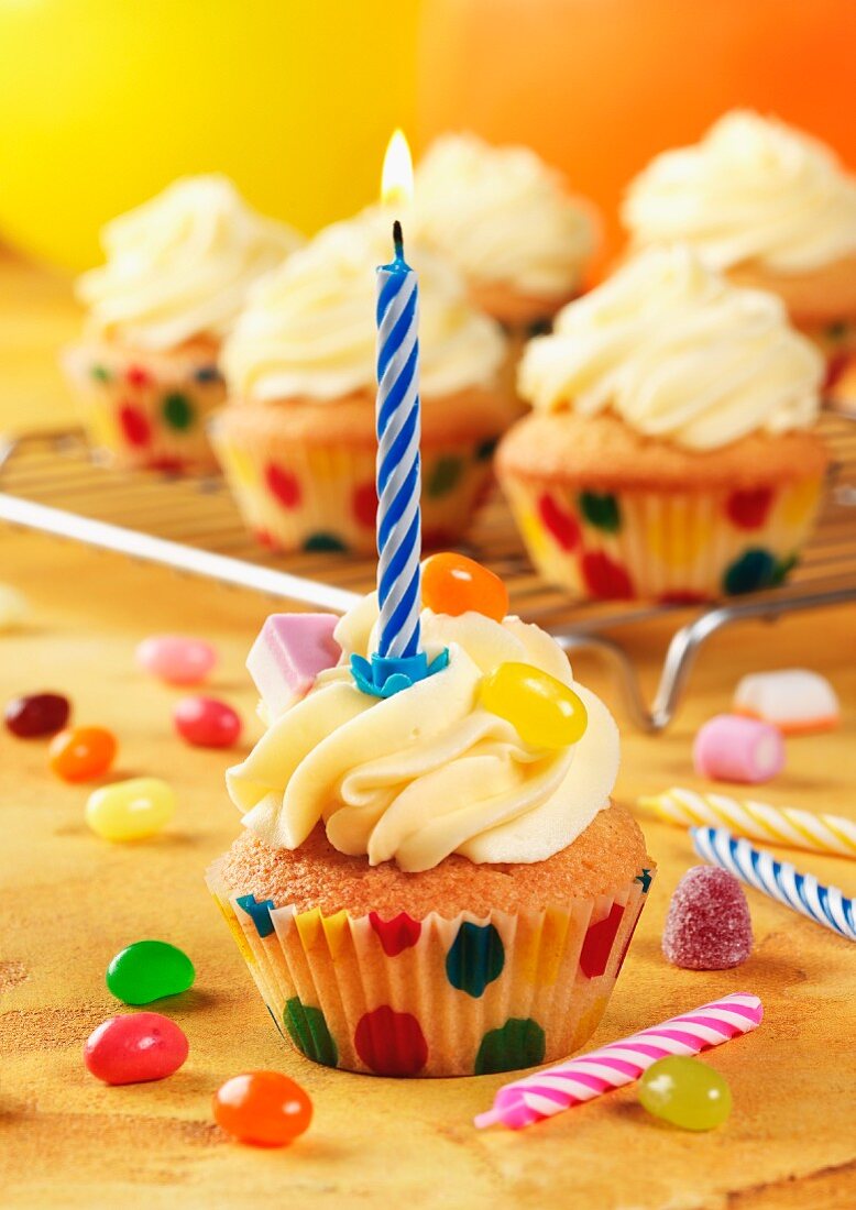 Birthday cupcakes, one in foreground with candle, 5 others on cooling rack in background