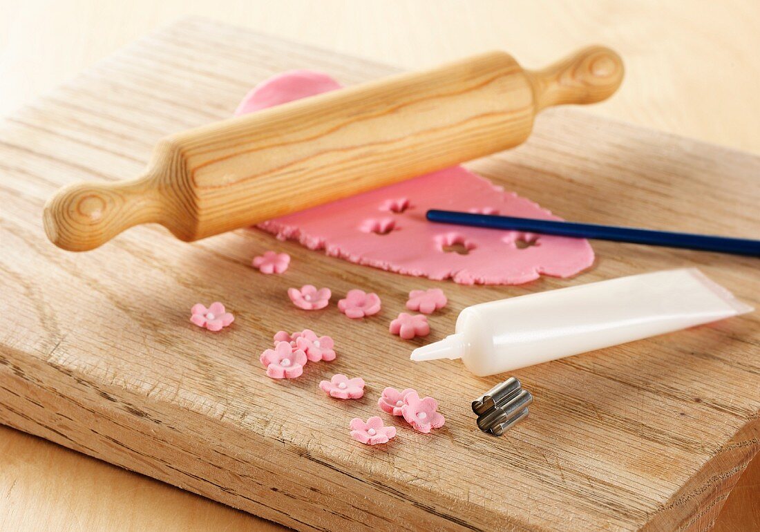 Pink icing rolled out on a board with rolling pin, showing a metal flower cutter and white icing tube