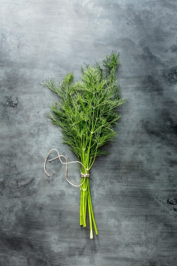 Bunch of dill stems tied with string on a grey stone surface