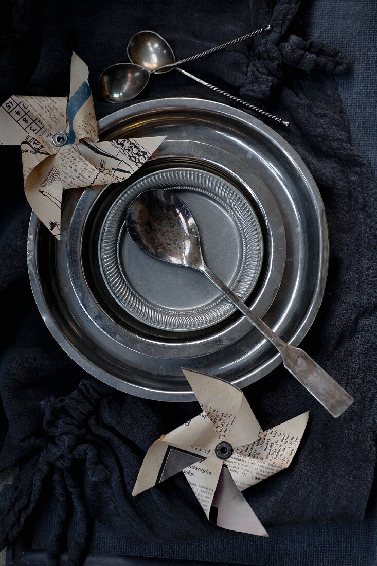 Metal plates, various spoons and newspaper windmills on black tablecloth