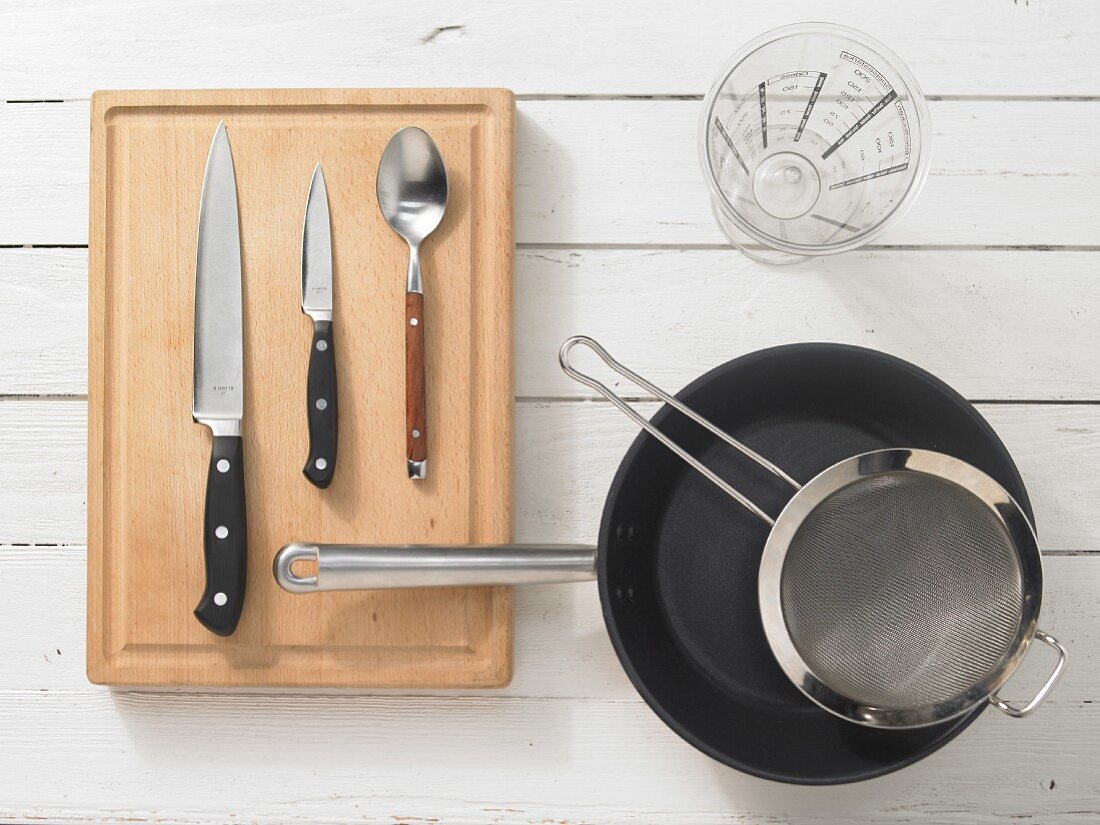 Various kitchen utensils: pan, sieve, measuring cup, knives, spoon
