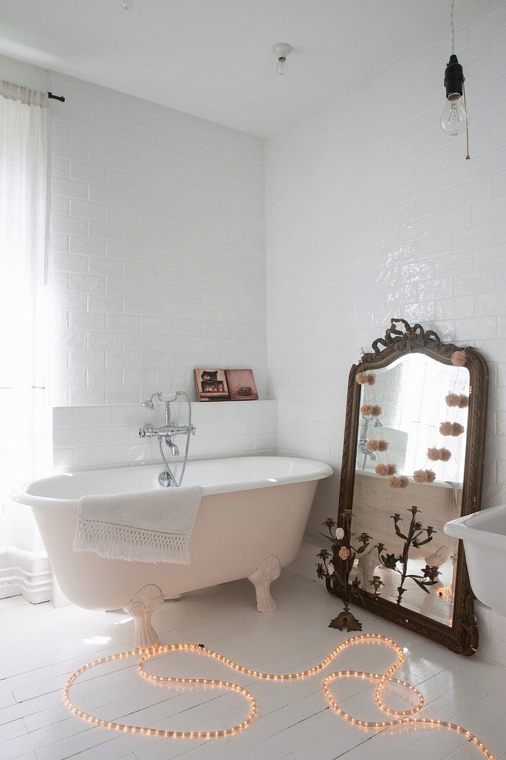 Rope light on floor next to free-standing bathtub and large mirror leant against wall in bathroom