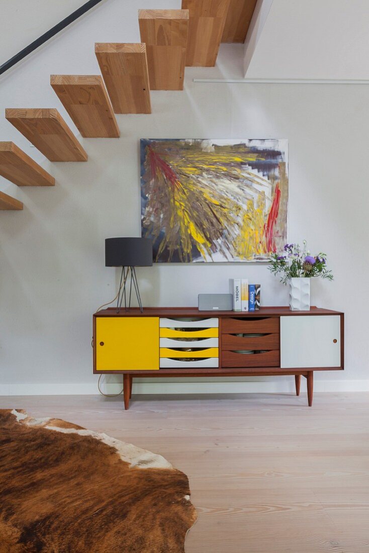 Abstract artwork above retro sideboard with colourful doors