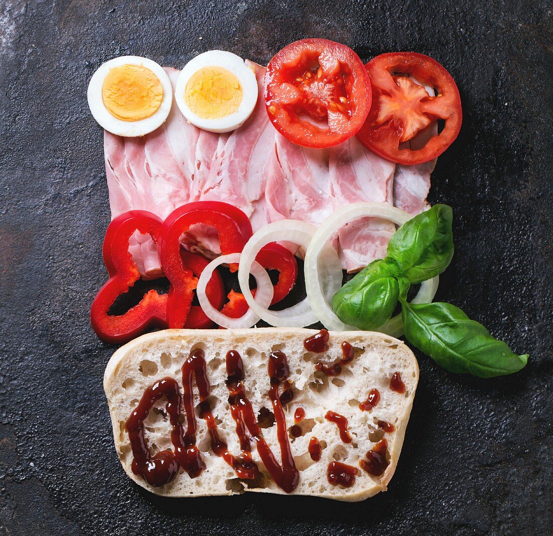 Ingredients for sandwich with ham, eggs, vegetables and ketchup over black background