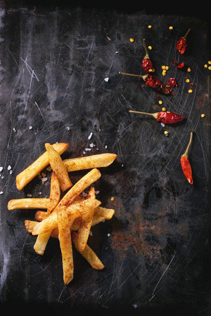 Fried potatoes with sea salt and red hot chili pepper over black metal surface