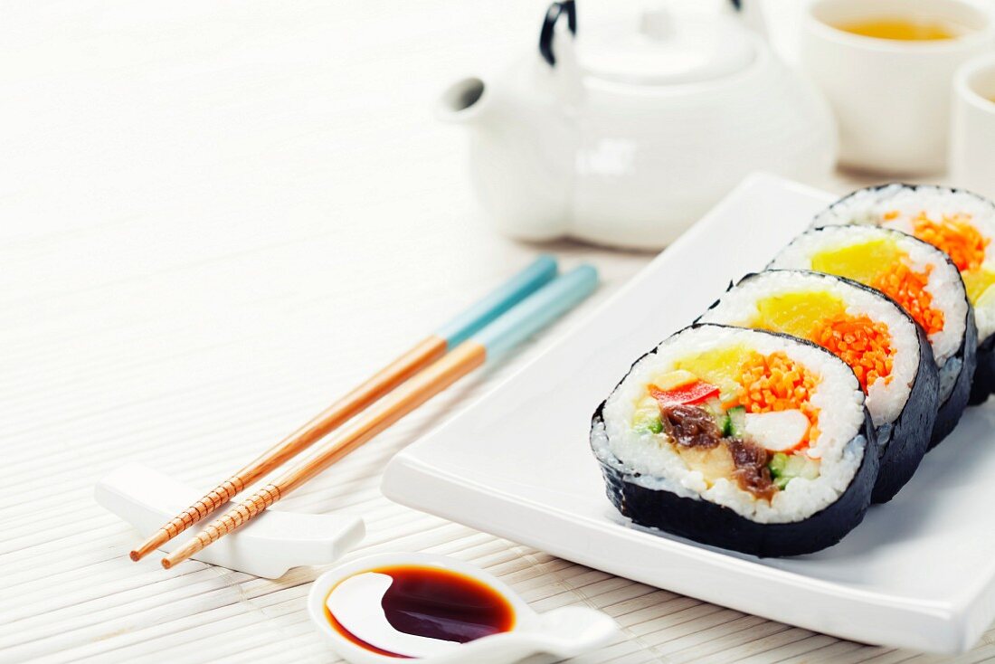 Maki-Sushi auf Servierplatte mit Stäbchen und Tee