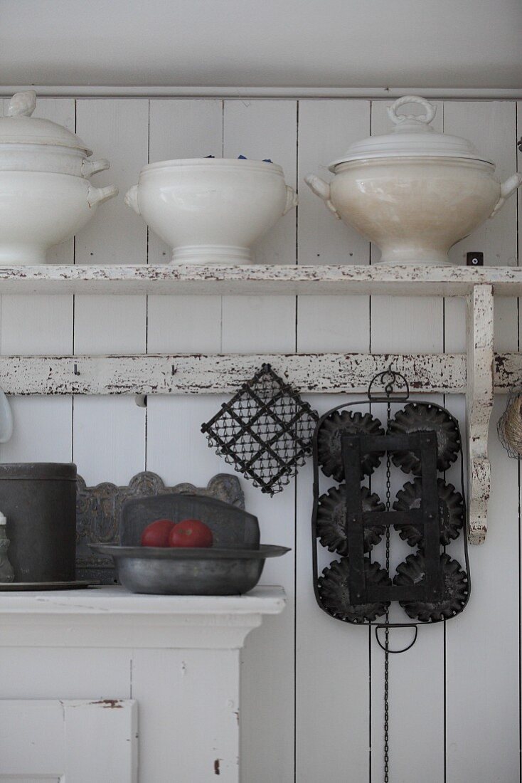 Old soup tureens on bracket shelf on white board wall