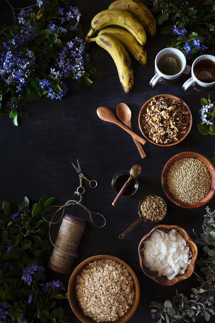 Ingredients for Banana Bread Granola on a dark surface, surrounded by fresh spring flowers
