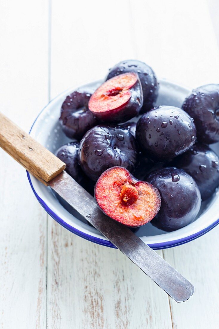Plums - Whole and sliced in a Bowl, on a white rustic background
