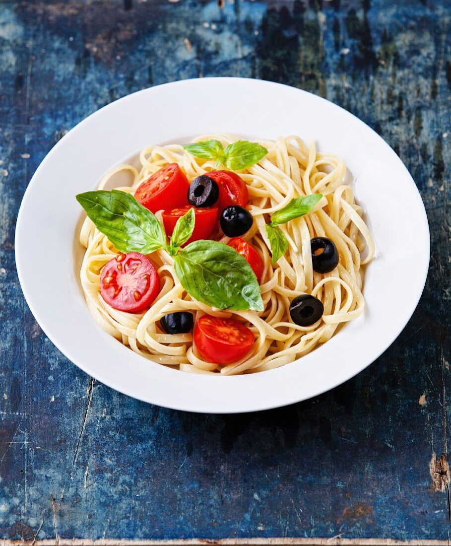 Pasta mit Tomaten, Basilikum und Oliven auf blauem Holzuntergrund