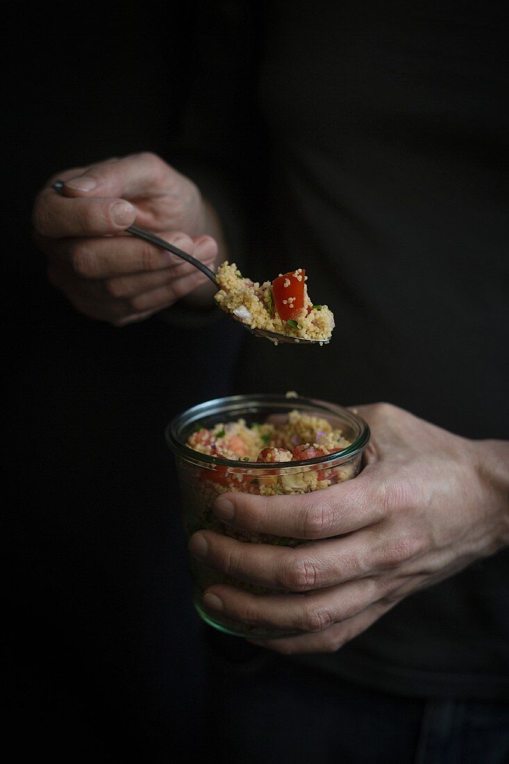 Hands holding a jar of couscous before dark background