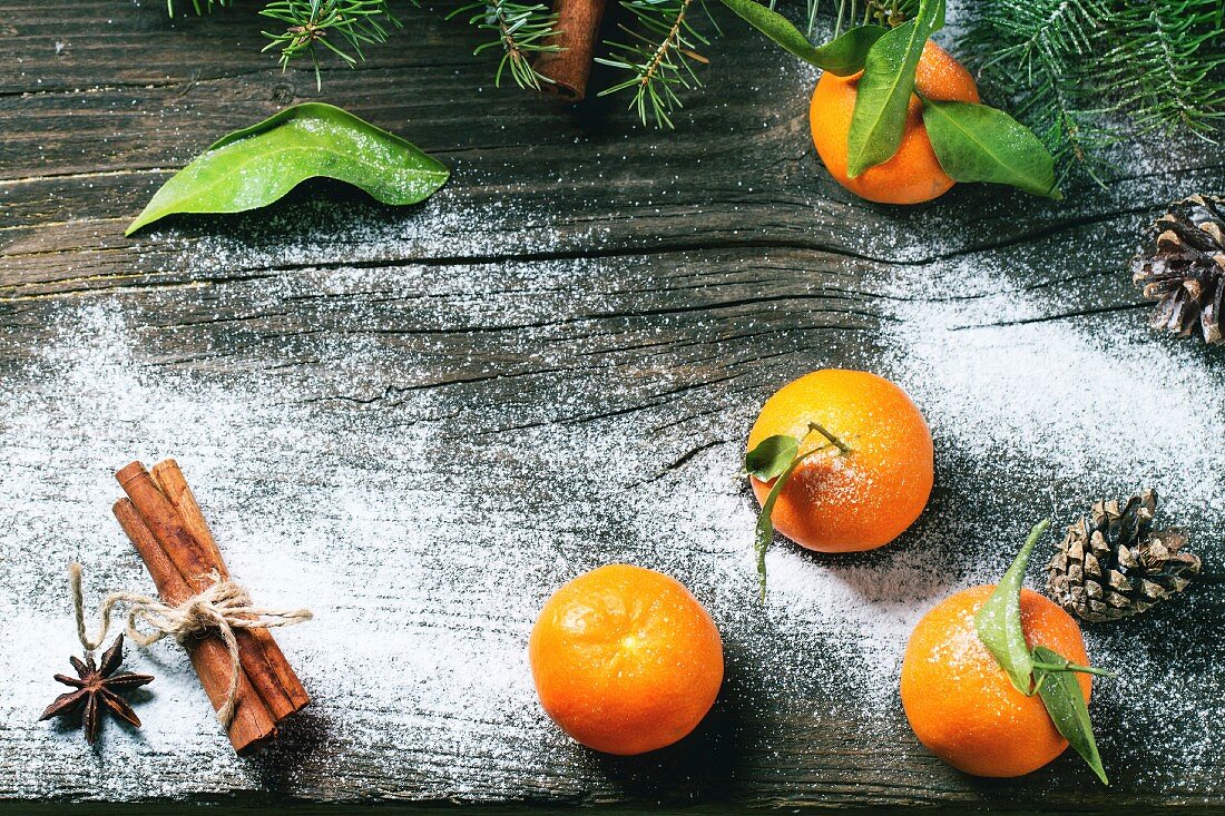 Stillleben mit Tangerinen, Zapfen und Gewürzen auf Holzuntergrund mit Schnee