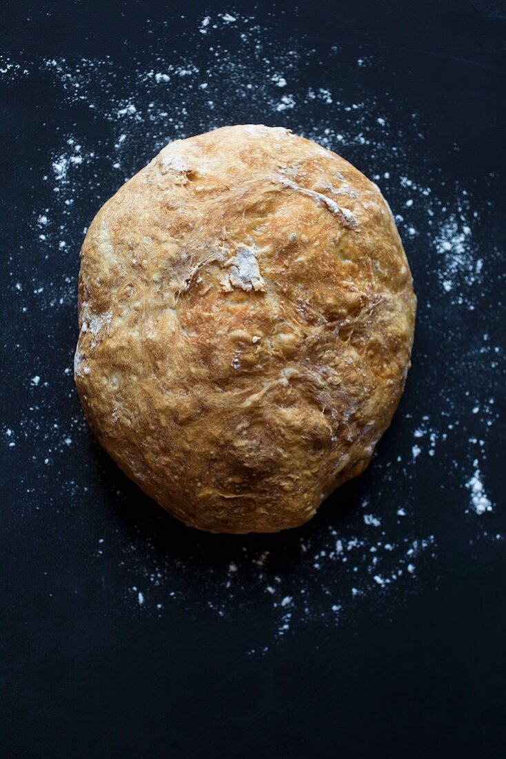Frisch gebackenes Brot mit Mehl vor dunklem Hintergrund (Aufsicht)