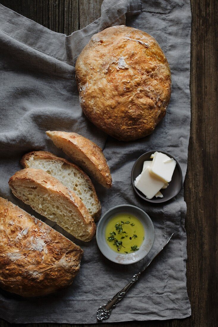 Brot, ganz und angeschnitten dazu Butter und Öl (Aufsicht)