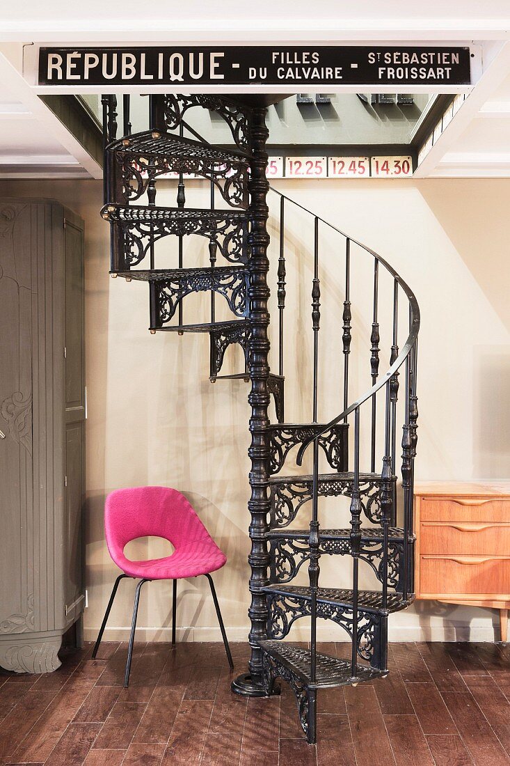 Pink retro chair next to black cast iron spiral staircase