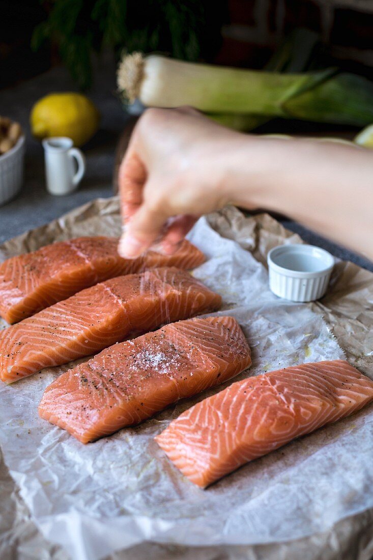 A woman is seasoning fresh salmon with salt and pepper