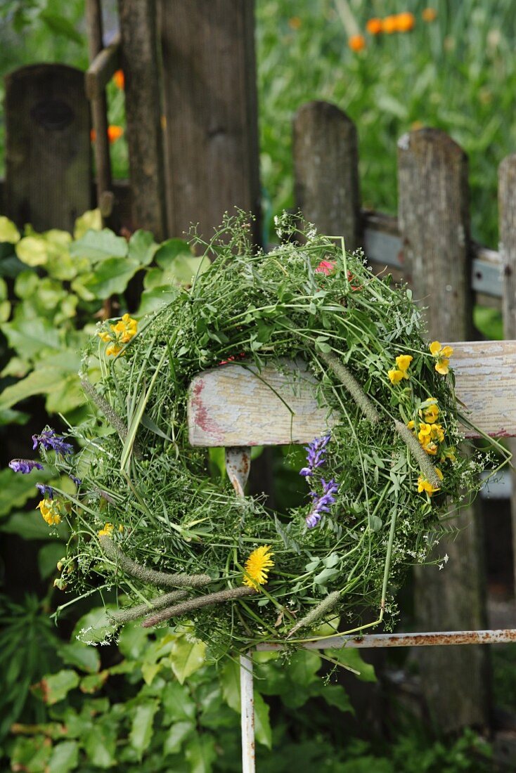 Wreath of wildflowers on backrest of vintage garden chair in front of weathered picket fence