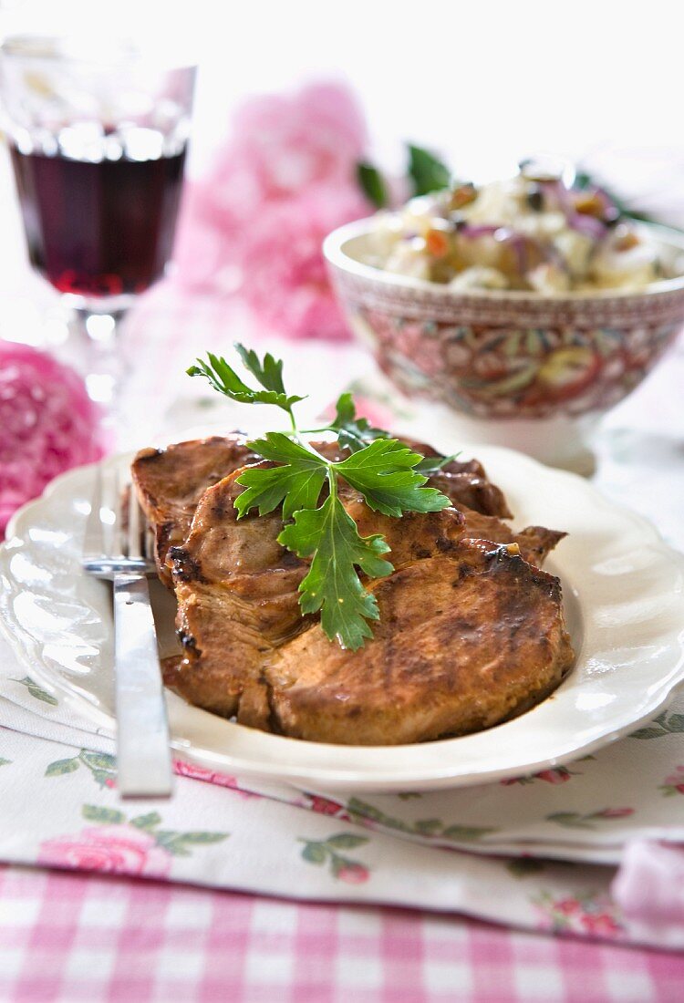 Gegrillte Schweinekoteletts mit Kartoffelsalat und einem Glas Rotwein