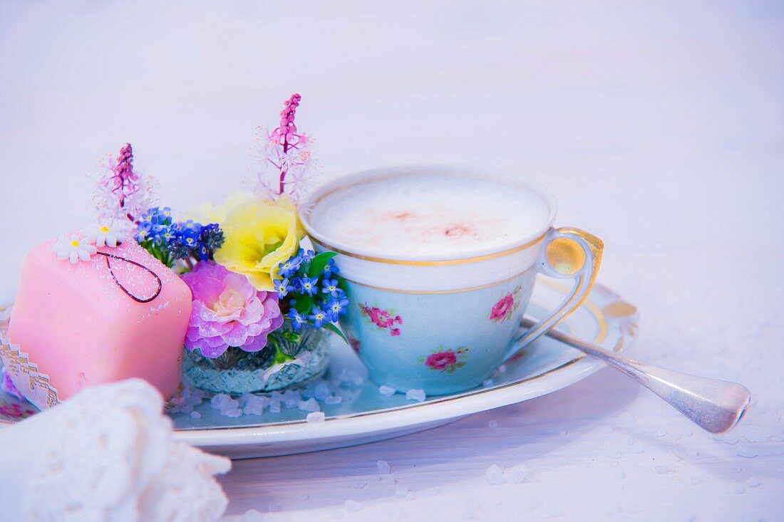 Cup of cappuccino, flower arrangement and petit four