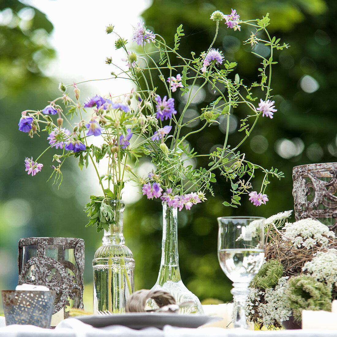 Delicate wildflowers in shades of purple in glass vases on set garden table