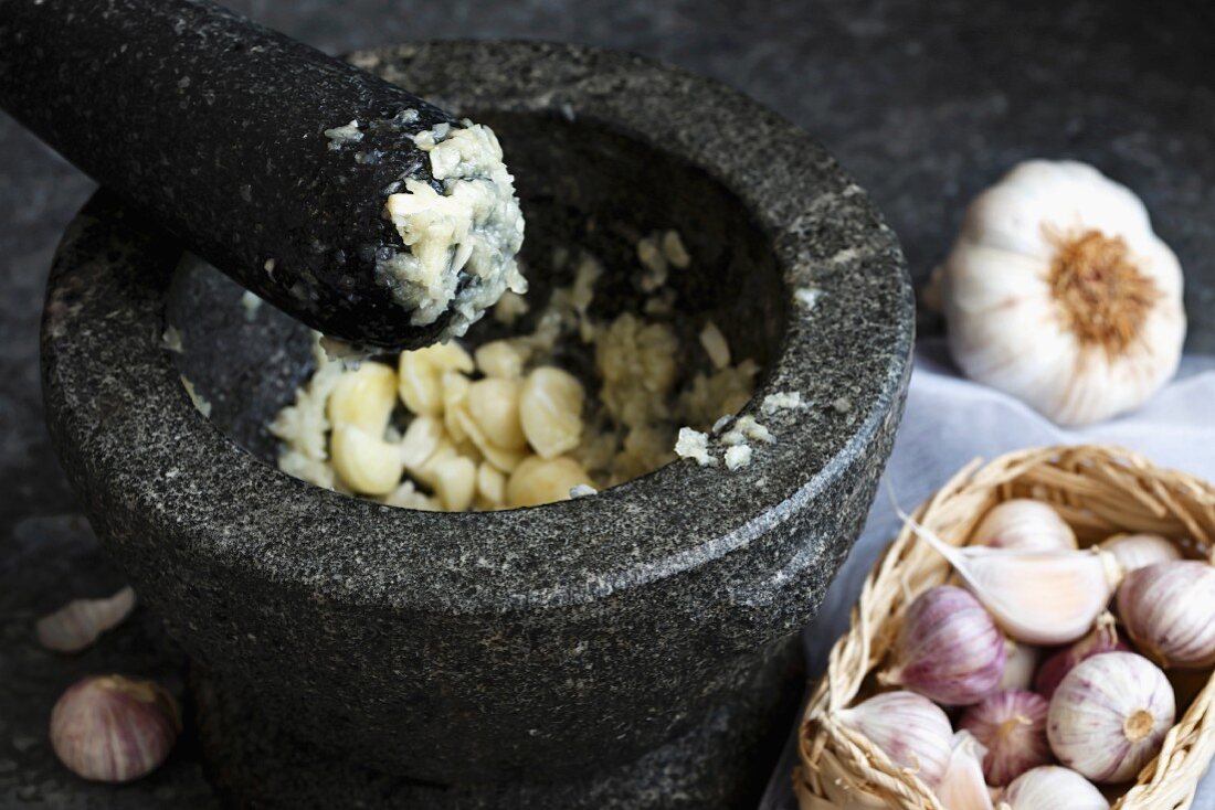 Mashed garlic in grey granite mortar with pestle, standing on dark sheet metal