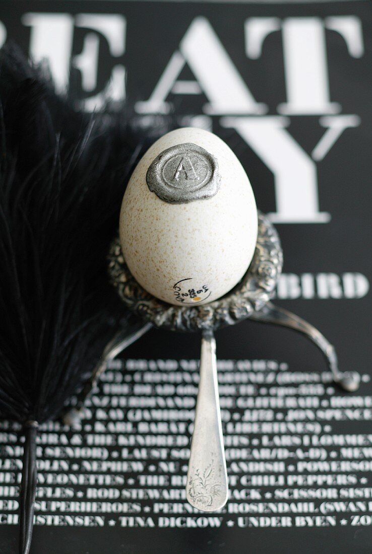 Ausgeblasenes Hühnerei mit Siegel auf Silbergefäß und schwarzweiß beschriftetem Hintergrund