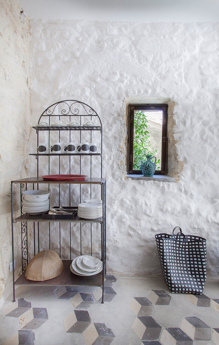 Ornate metal shelves next to small window in plastered stone wall