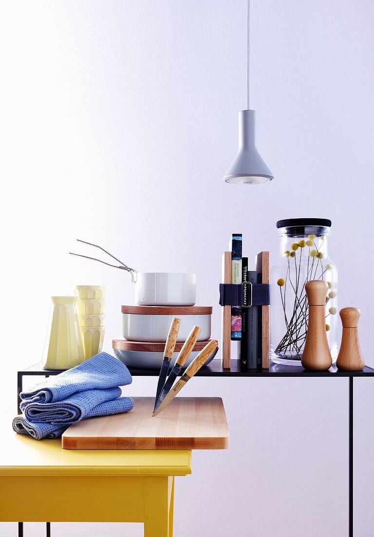 Yellow kitchen table, chopping board and knives in front of cooking utensils and books on delicate metal table