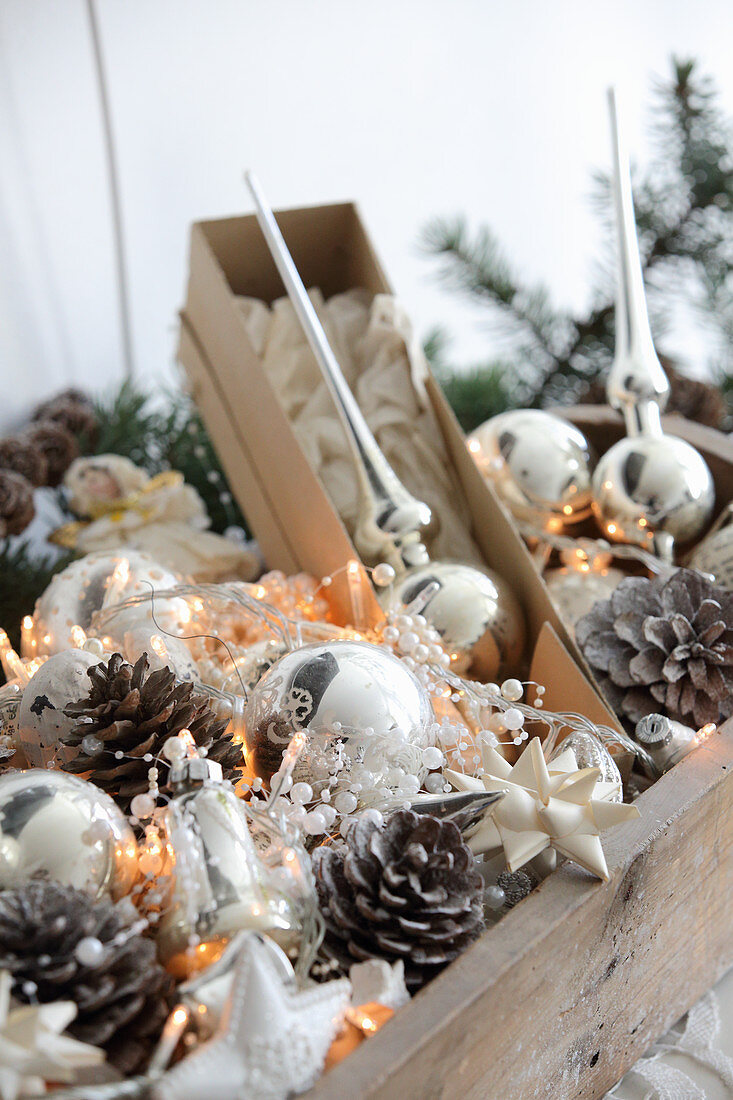 Silver Christmas tree baubles, pine cones and fairy lights in wooden crate