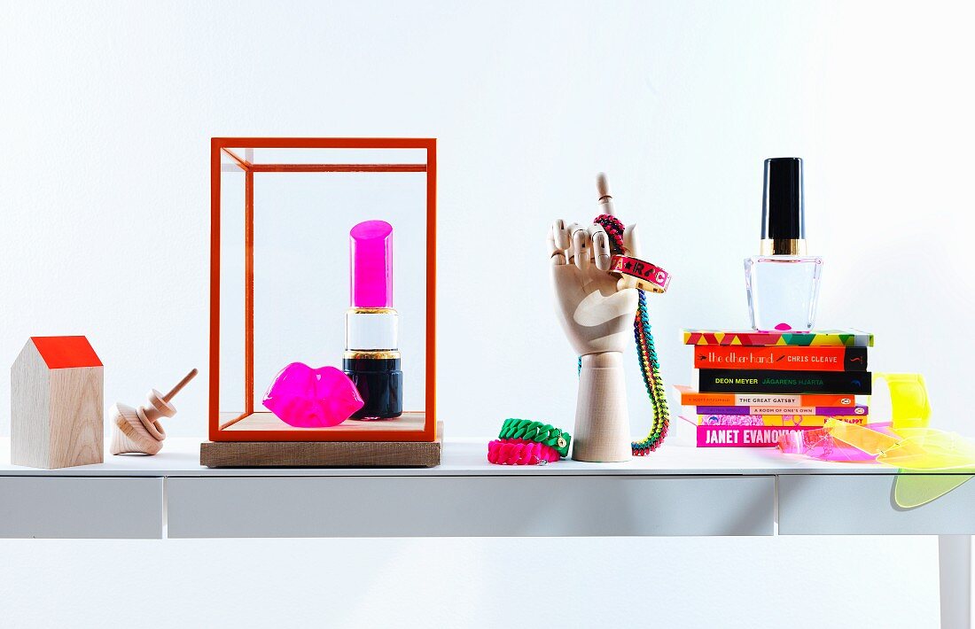 Feminine, neonfarbene Accessoires und Bücherstapel auf weißem, filigranem Schubladentisch