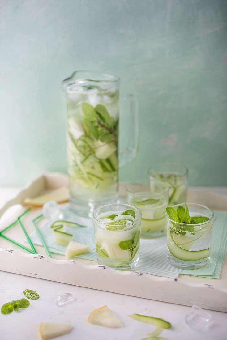 A jug and glasses of refreshing cucumber and melon water with fresh mint for summer.