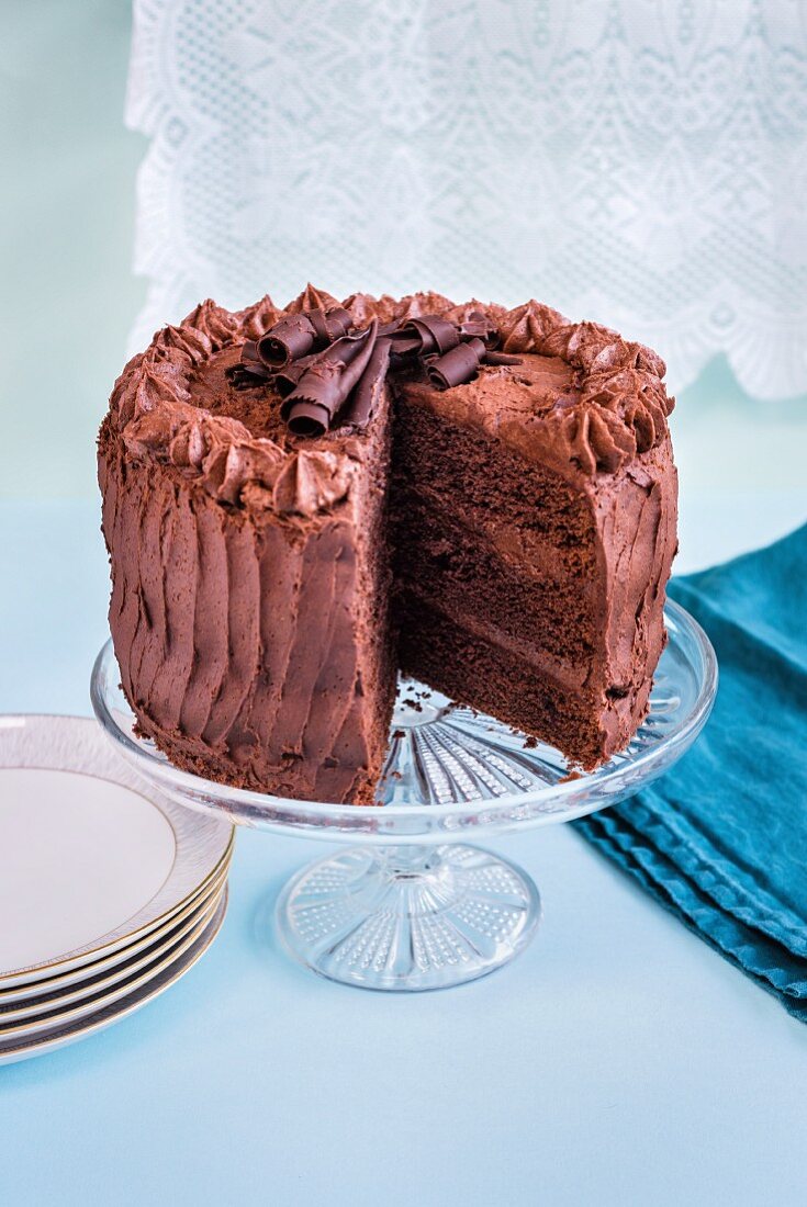 Chocolate layer cake with slice taken out on glass cake stand
