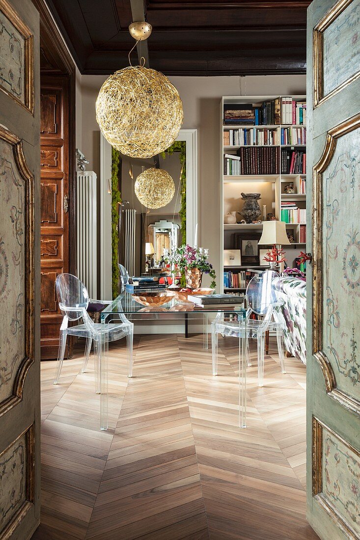 View of transparent furniture in library seen through antique, painted, panelled doors
