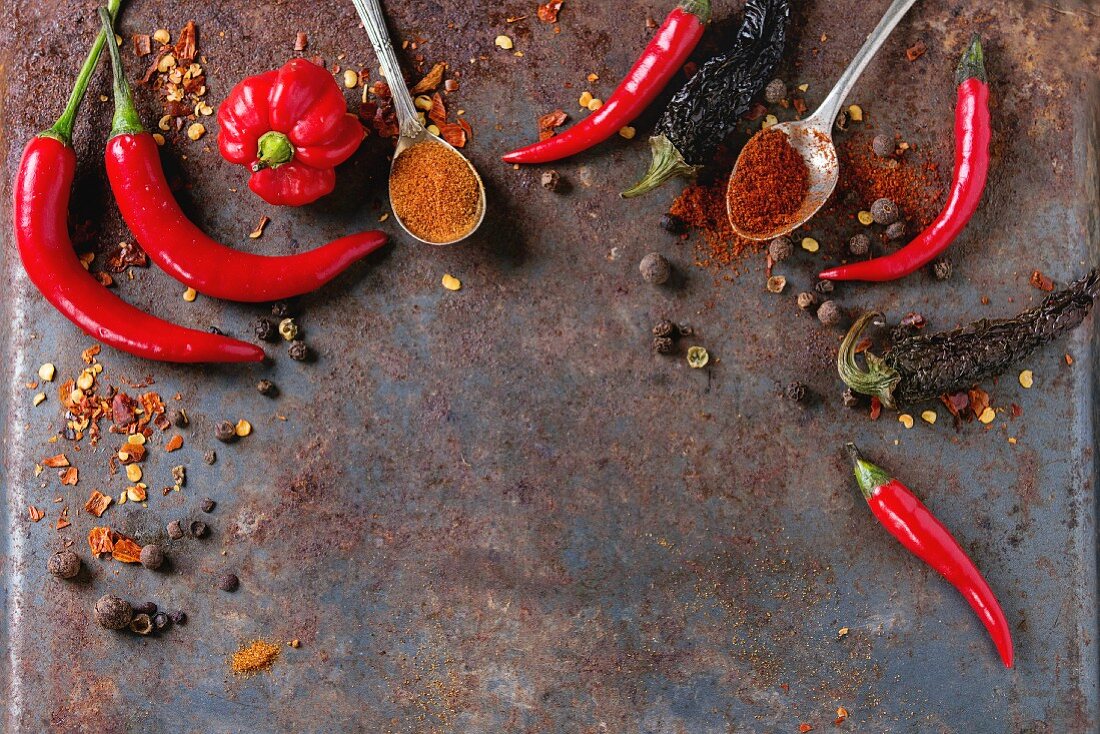 Spicy background with assortment of different hot chili and allspice peppers over old rusty iron background