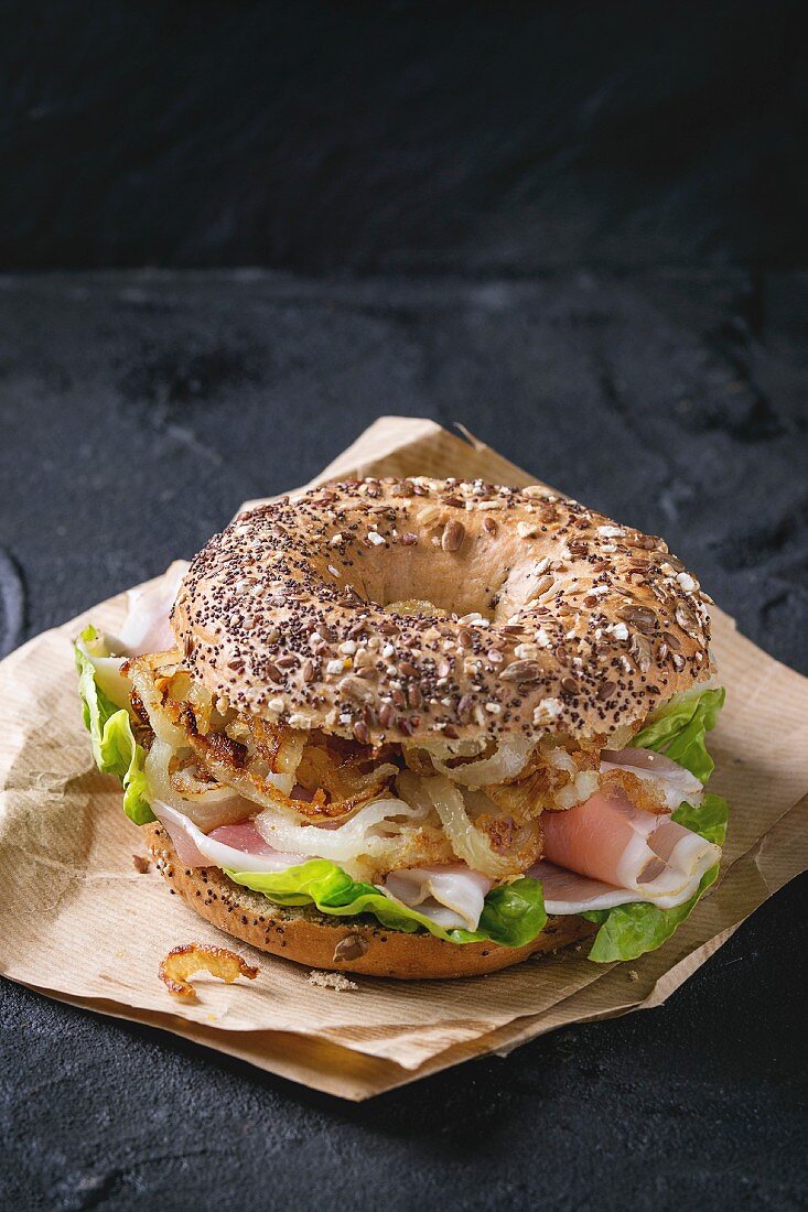 Whole Grain bagel with fried onion, green salad and prosciutto ham on paper