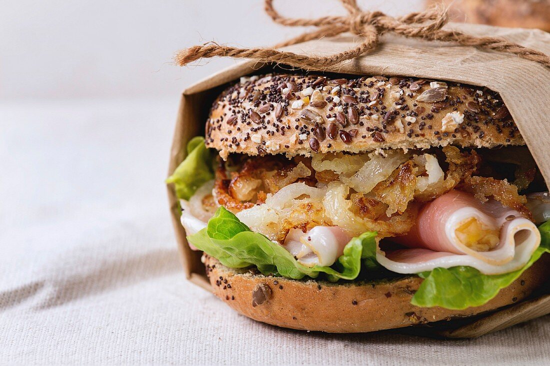 Vollkorn-Bagel mit gebratenen Zwiebeln, Salat und Schinken in Papier gewickelt